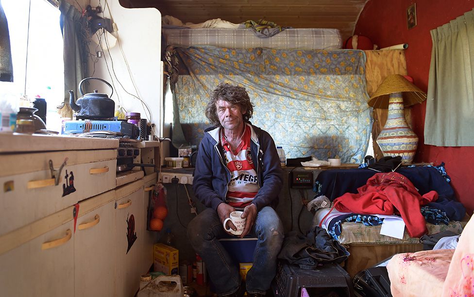 A man clutches a mug as he sits in his home