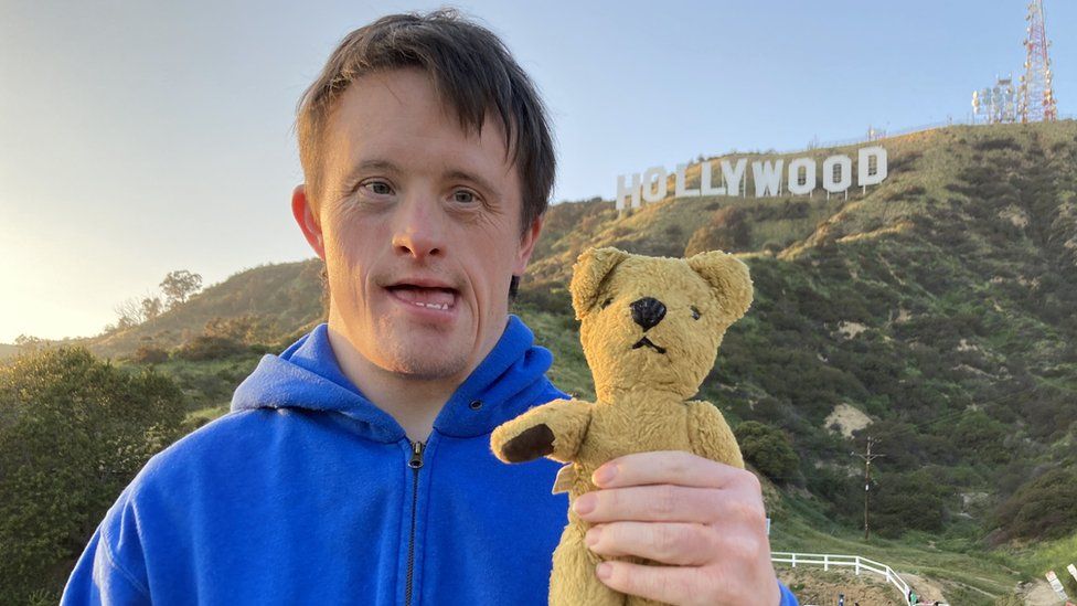 Tommy Jessop holding Roger the bear, in front of the Hollywood sign
