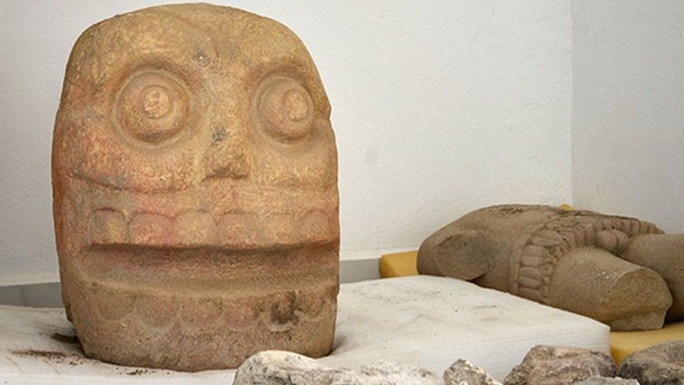 A large stone head and a torso of the God pictured on display