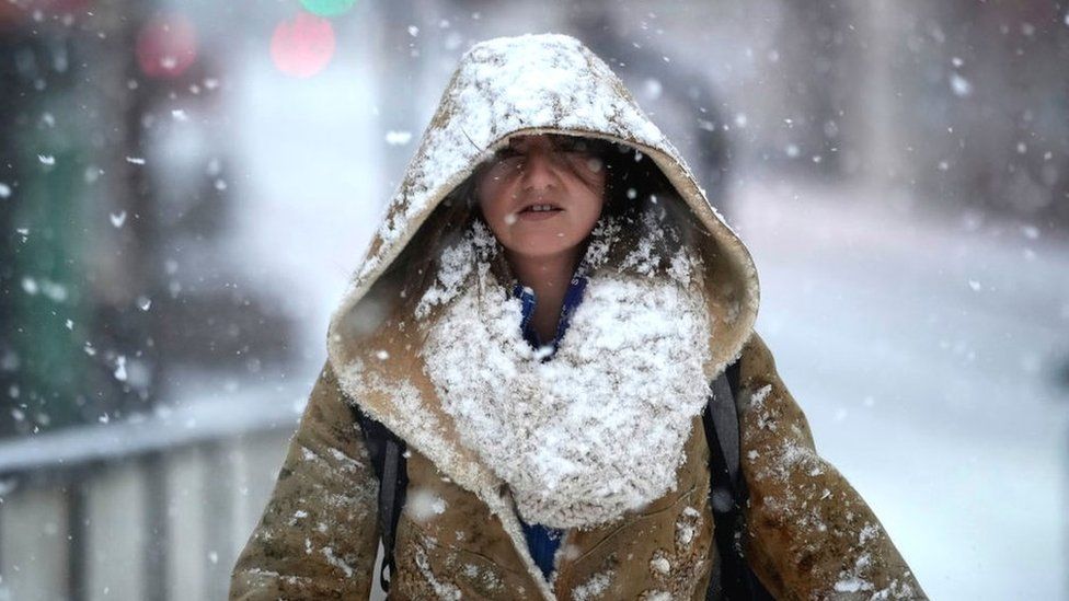 A Woman Covered In Snow Walks Down The Street