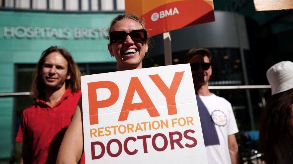 Фотография бастующего врача в очках с плакатом «Восстановление зарплаты врачам»