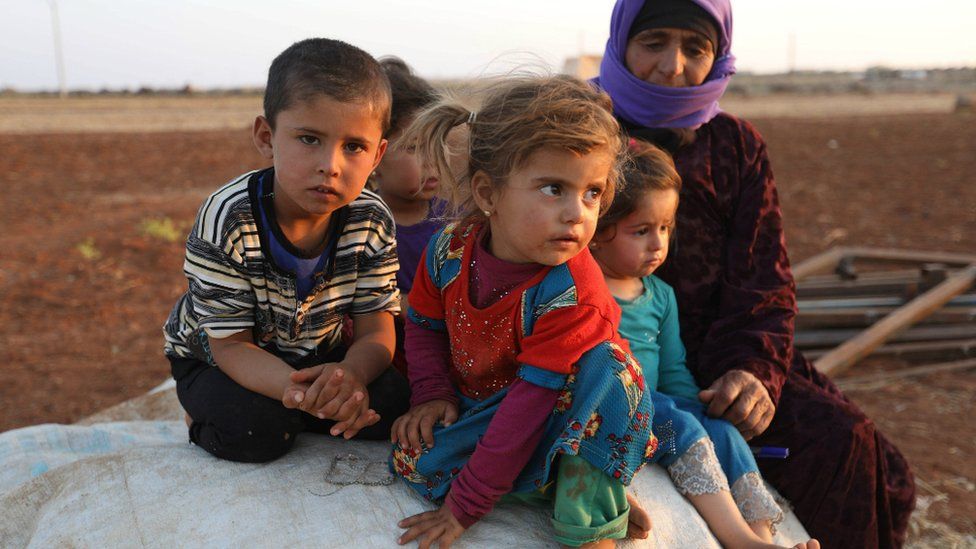 Syrian children sit next to a woman at a camp for displaced civilians near the village of Sarman in Idlib province on September 1, 2018