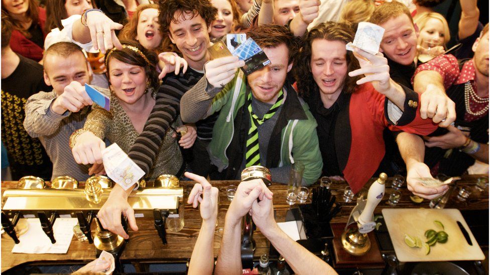Drinkers in a busy pub try and get bartender's attention