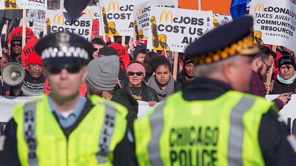 Police keep watch as demonstrators demanding an increase in the minimum wage to $15-dollars-per-hour march in the streets on April 14, 2016 in Chicago