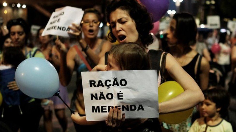 A woman holds up a placard reading "food pellets are not a meal" during a protest