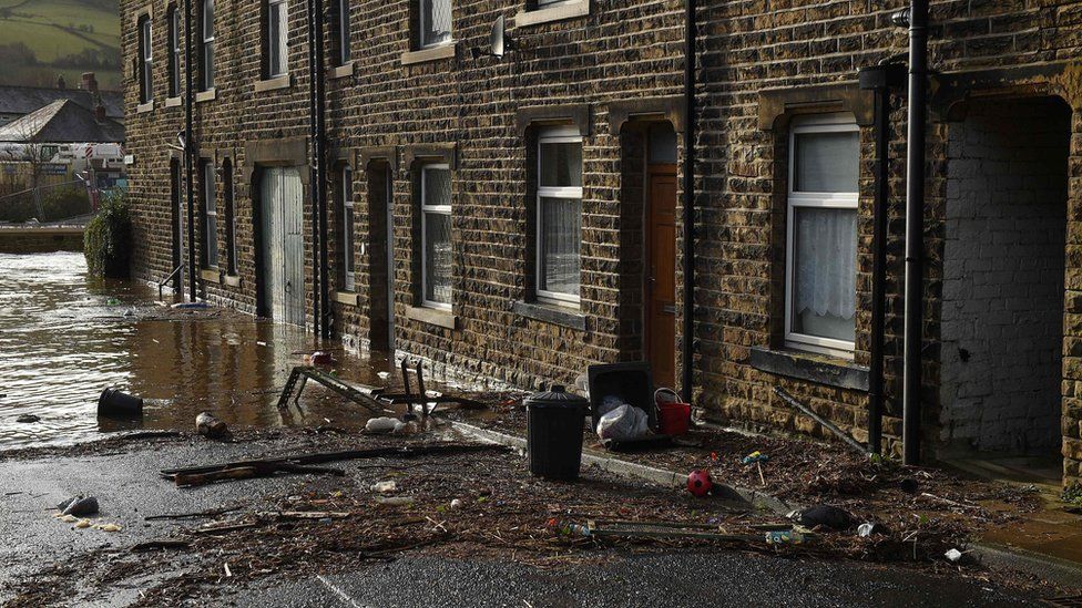 Debris from flood water litters the street outside houses in Mytholmroyd