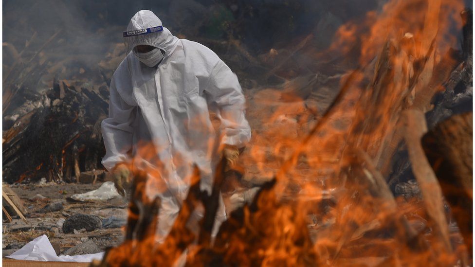 A Family member, wearing a Personal Protective Equipment (PPE), performs the last rites for COVID-19 victims