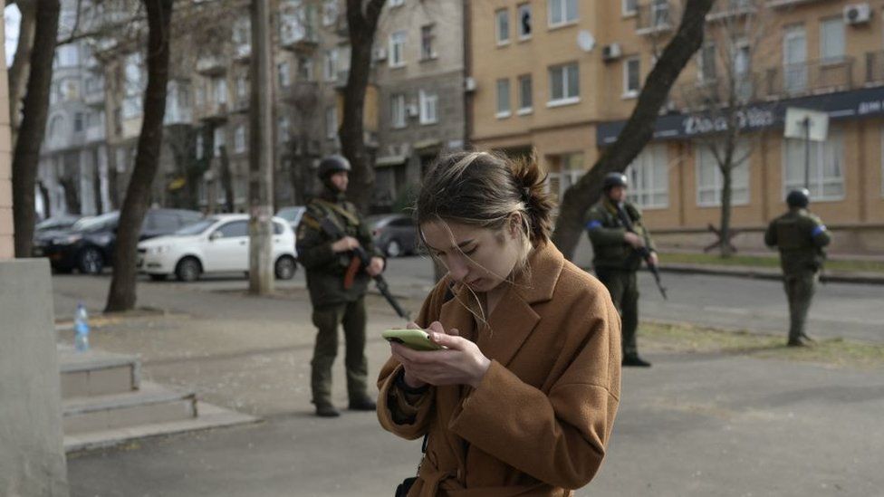 Woman on a mobile phone standing in front of Ukrainian soldiers