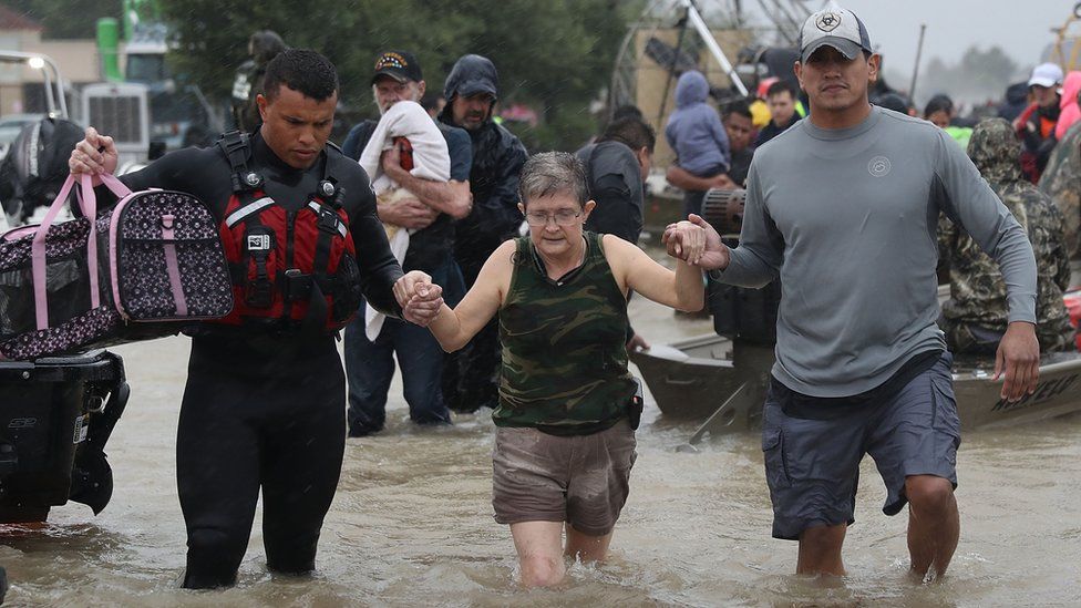 A woman is led through flood waters to safety after Hurricane Harvey