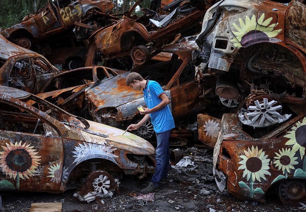 Украины зураач Вячеслав Рыбка 2022 оны 8-р сарын 10-нд Оросын Ирпин хотод довтлох үеэр сүйрсэн машиныг зурж байна.