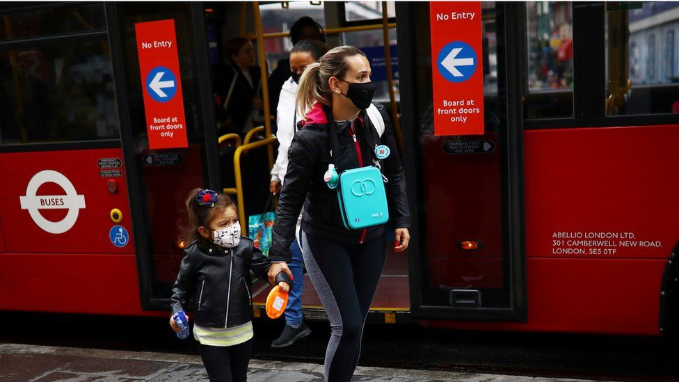 A woman and a child are seen wearing a protective face mask by a London bus