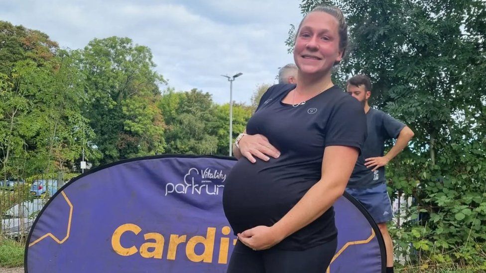 Zoe holding her baby bump in front of a Parkrun sign