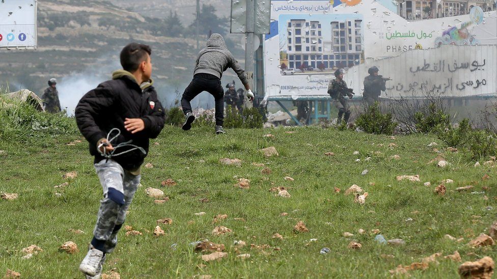 Palestinian protesters seek cover during clashes marking Land Day in the West Bank City of Ramallah, 30 March 2018