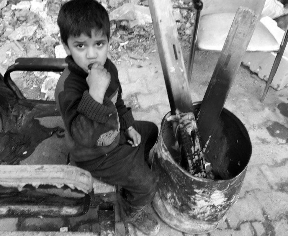 Boy eats a cucumber as he sits next to a fire in eastern Aleppo
