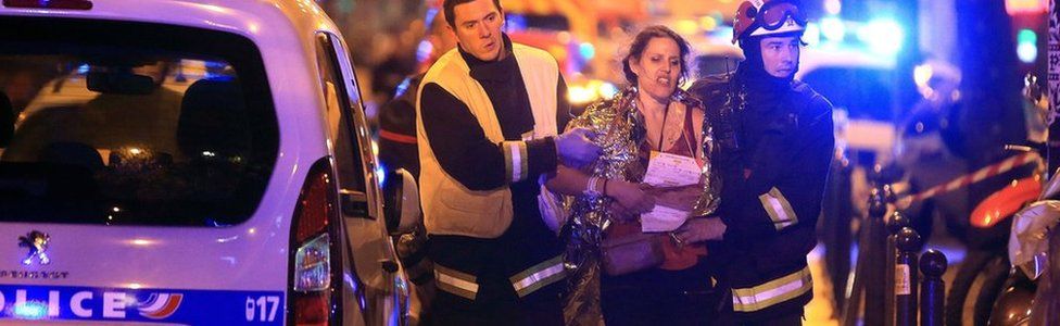 Rescue workers help a woman after a shooting, outside the Bataclan theatre in Paris