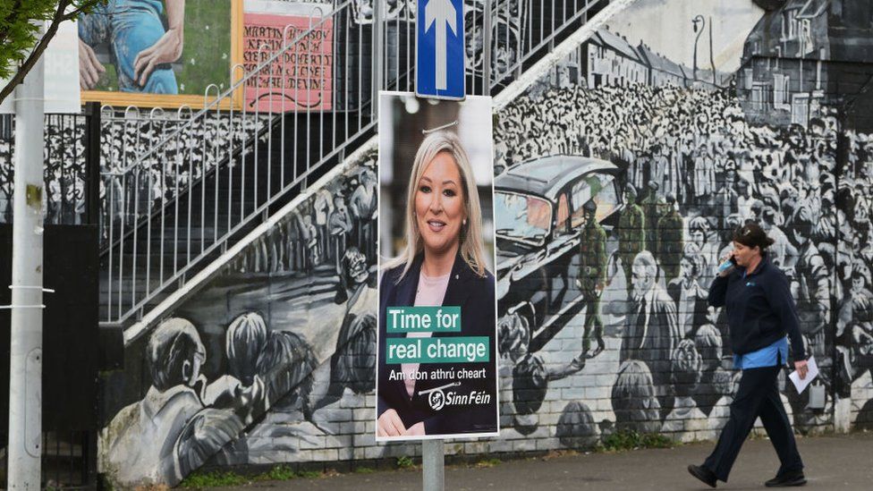 Sinn Féin's Michelle O'Neill election poster is seen against the backdrop of a republican mural in the nationalist area of west Belfast