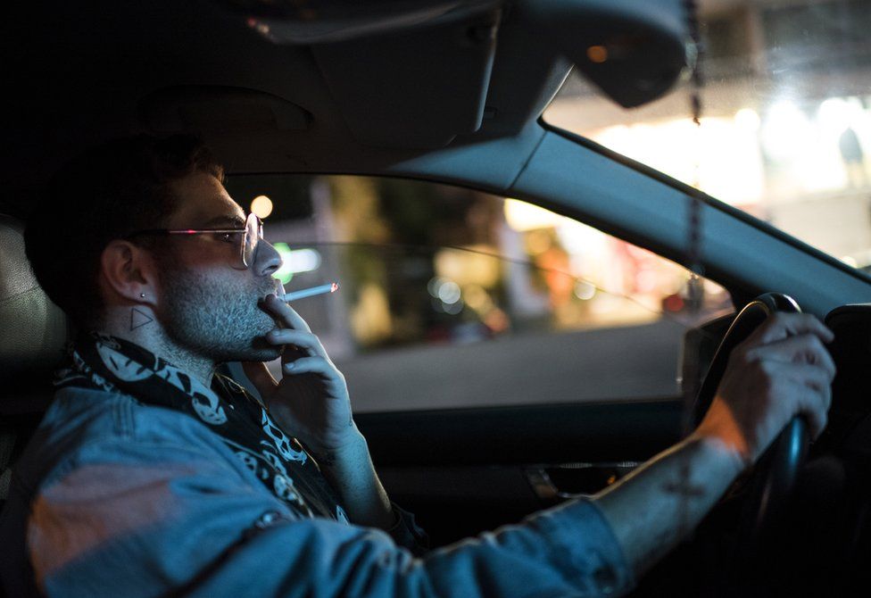 Elias smokes a cigarette whilst driving