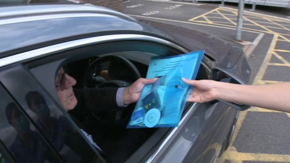 Patient in a car being handed a blue folder containing a device and documents