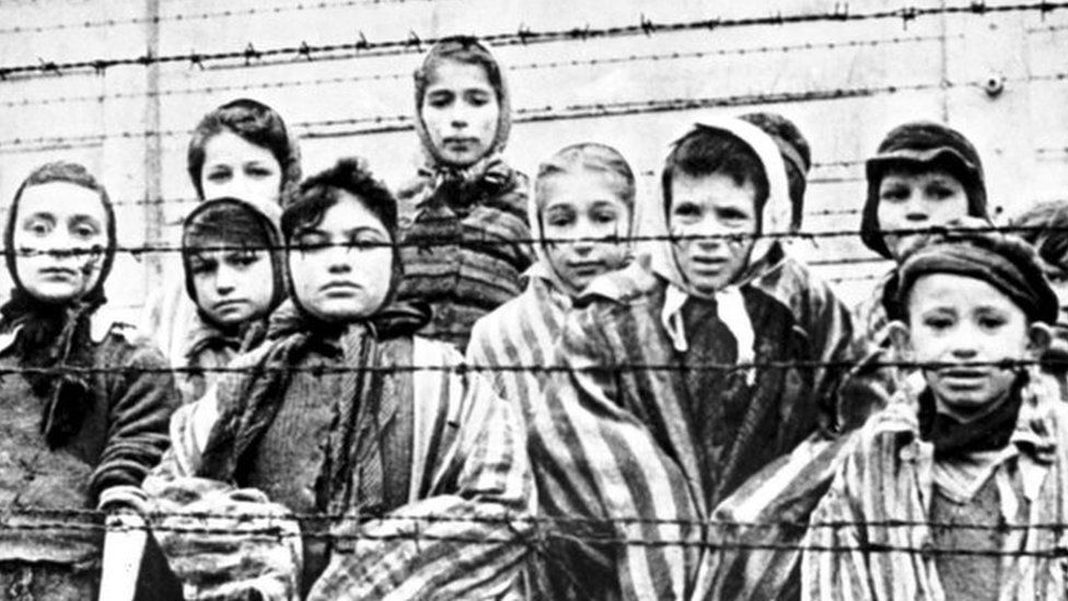 A group of child survivors behind a barbed wire fence at the Nazi concentration camp at Auschwitz-Birkenau in southern Poland, 27 January 1945