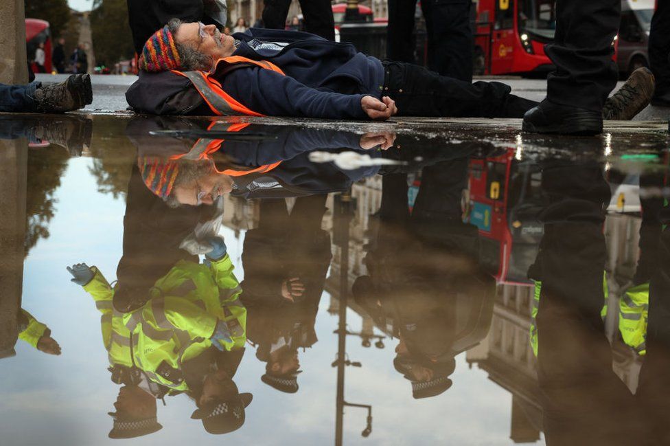 A Just Stop Oil climate activist, lying on the ground, is detained by a police officer, seen reflected in a rain puddle, after taking part in a slow march to disrupt traffic, in Parliament Square in London on October 30, 2023.