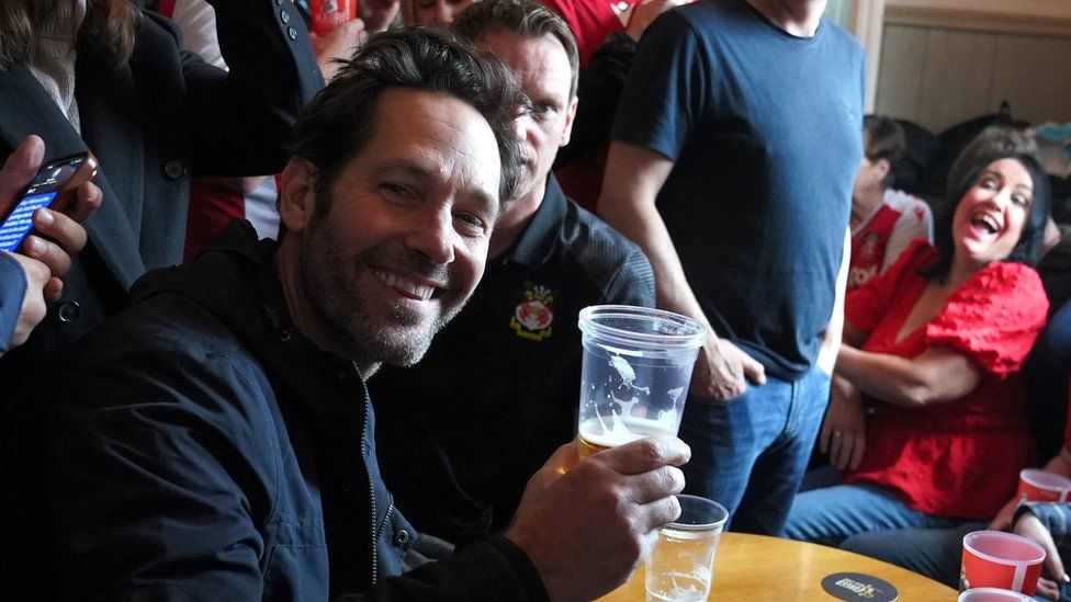 Paul Rudd raising a pint glass in the Turf pub in Wrexham before Wrexham FC's game against Boreham Wood