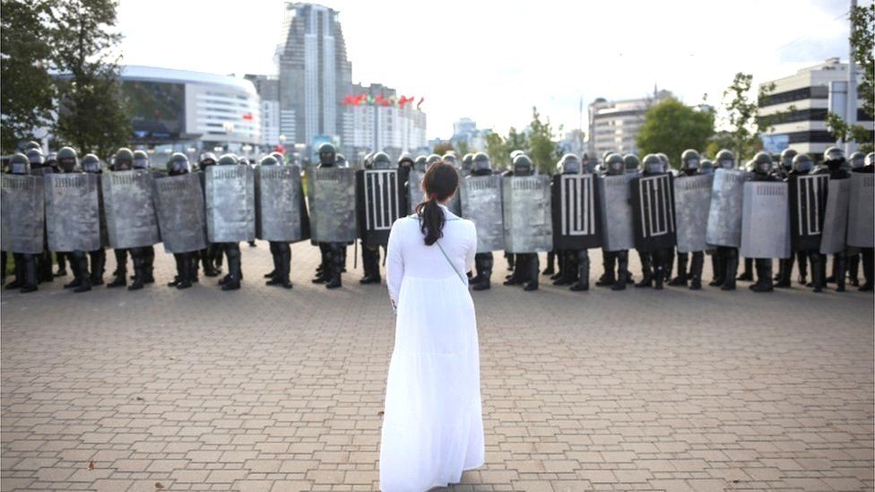 Woman in white facing line of riot police