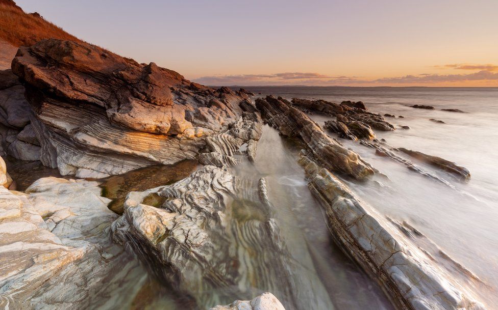 Waves lap over rocks as the sun rises at Bloody Bridge, near Newcastle in County Down