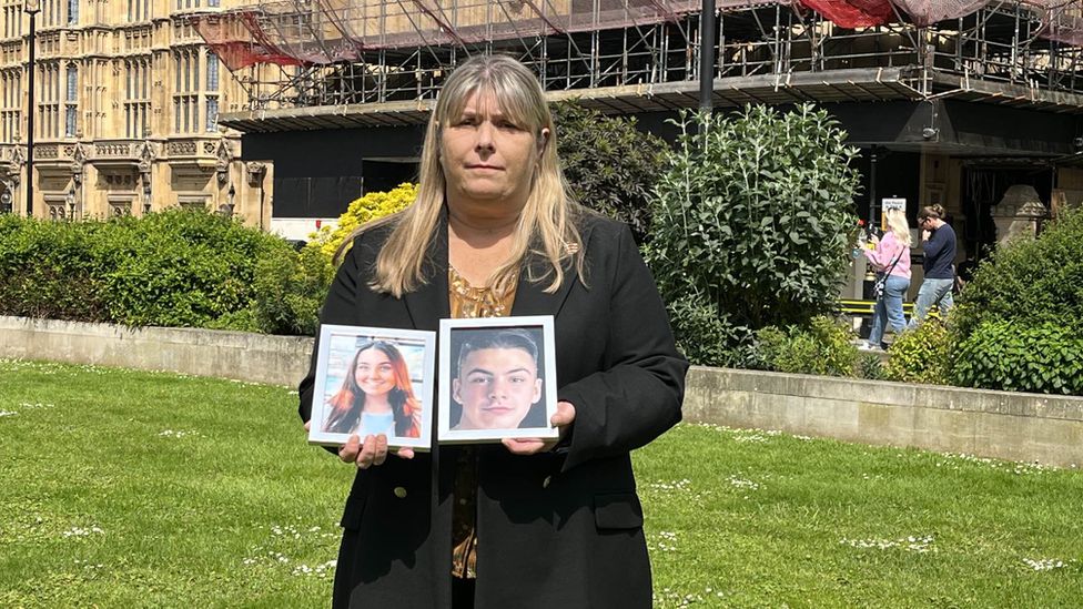 Julie Taylor standing outside the Houses of Parliament. She is holding two pictures, one of her grandson Liam Taylor and the other of