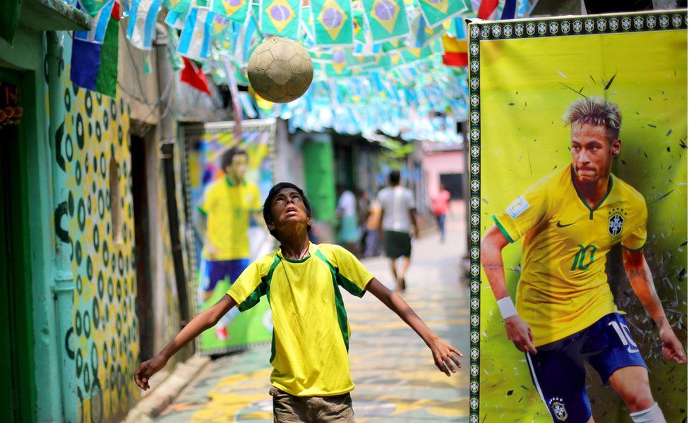 An Indian boy dribbles a ball next to a poster of Brazilian footballer Neymar in a lane decorated with Brazilian flags in Kolkata on 2 July 2018.