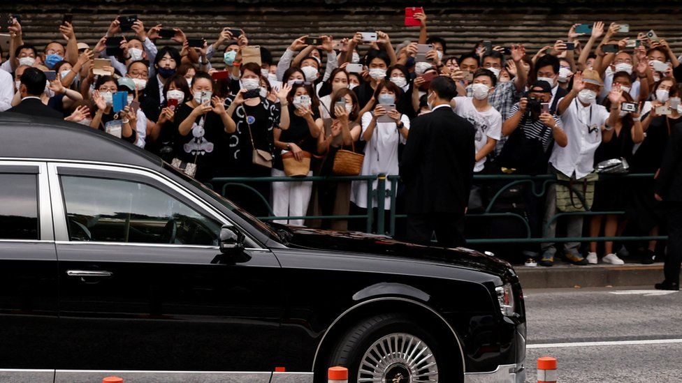 Люди смотрят, как машина с телом бывшего премьер-министра Японии Синдзо Абэ, застреленного во время предвыборной кампании, уезжает после его похорон в храме Дзодзёдзи в Токио, Япония, 12 июля 2022 года.