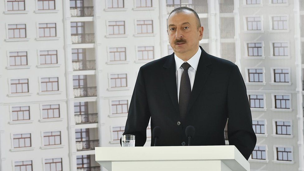 President Ilham Aliyev giving a speech in front of a picture of the flats