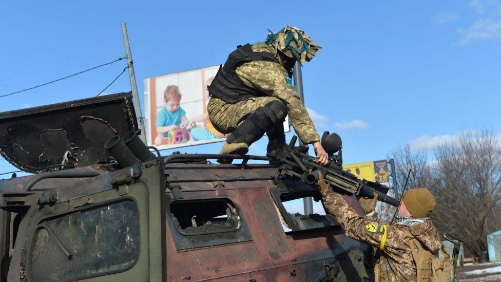 An Ukrainian Territorial Defence fighter takes the automatic grenade launcher from a destroyed Russian infantry mobility vehicle GAZ Tigr after the fight in Kharkiv on February 27, 2022.