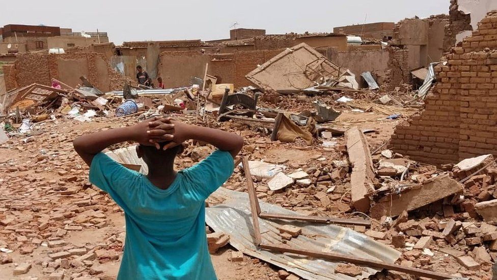 A child stands in front of damaged buildings following fighting in Sudan