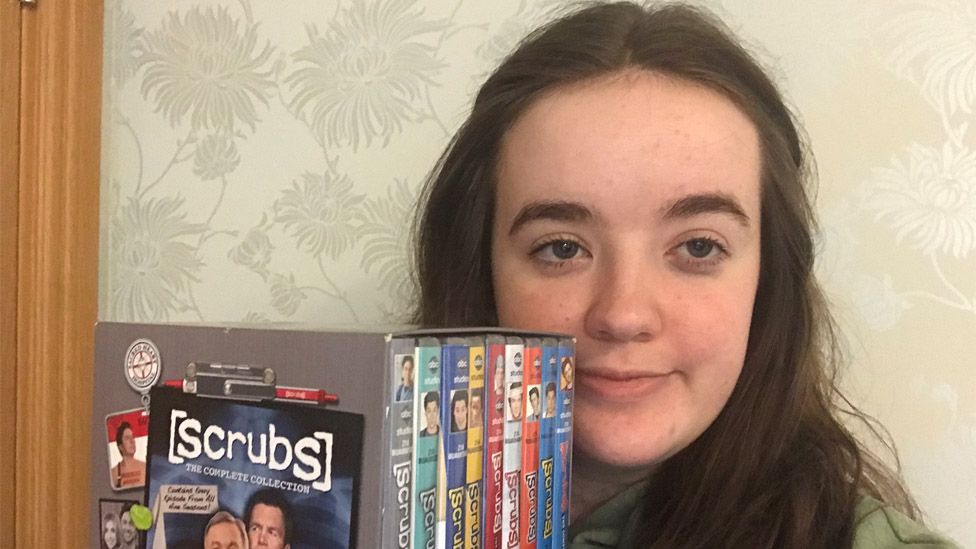 Clara holding a box set of Scrubs on DVD