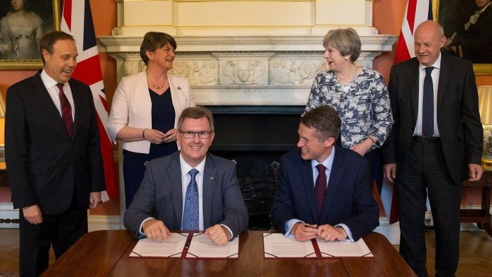 DUP MP Jeffrey Donaldson and Tory Chief Whip Gavin Williamson sign the paperwork as DUP's deputy leader Nigel Dodds, leader Arlene Foster, PM Theresa May and First Secretary of State Damian Green look on.