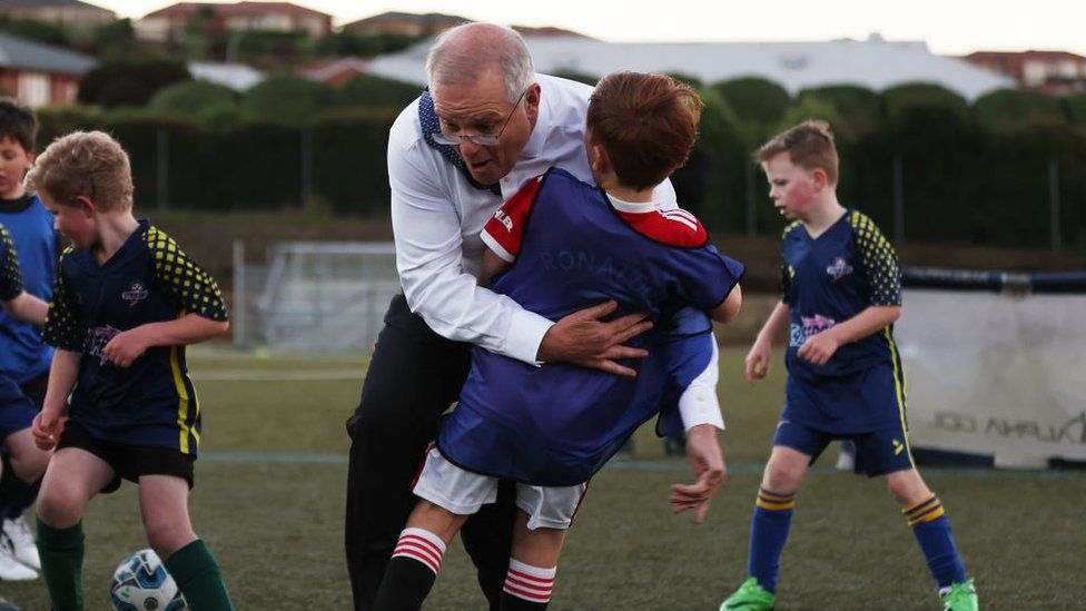 Scott Morrison knocks over a child while playing a game of soccer