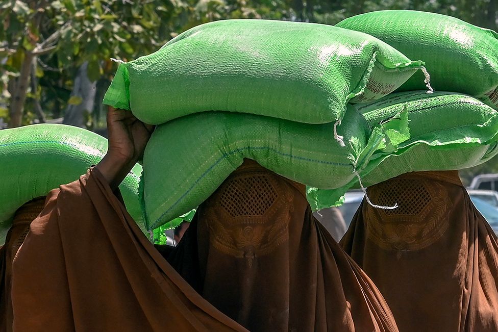 Women carry free bags of flour from a government distribution point in Peshawar, Pakistan, on 10 April 2023