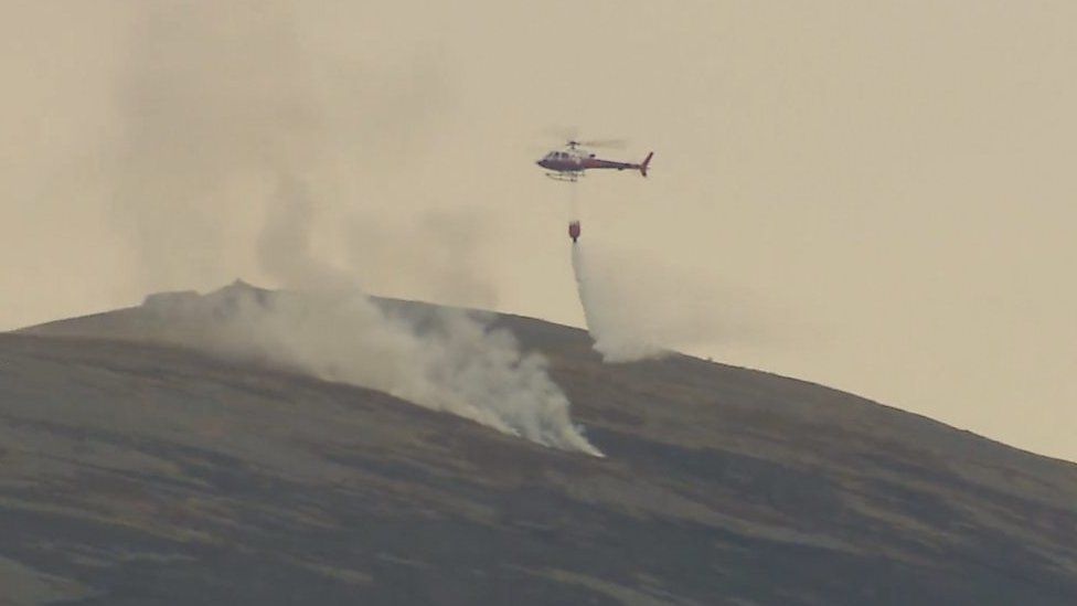 Plumes of smoke billowed into the sky as helicopter drops water on the fire below