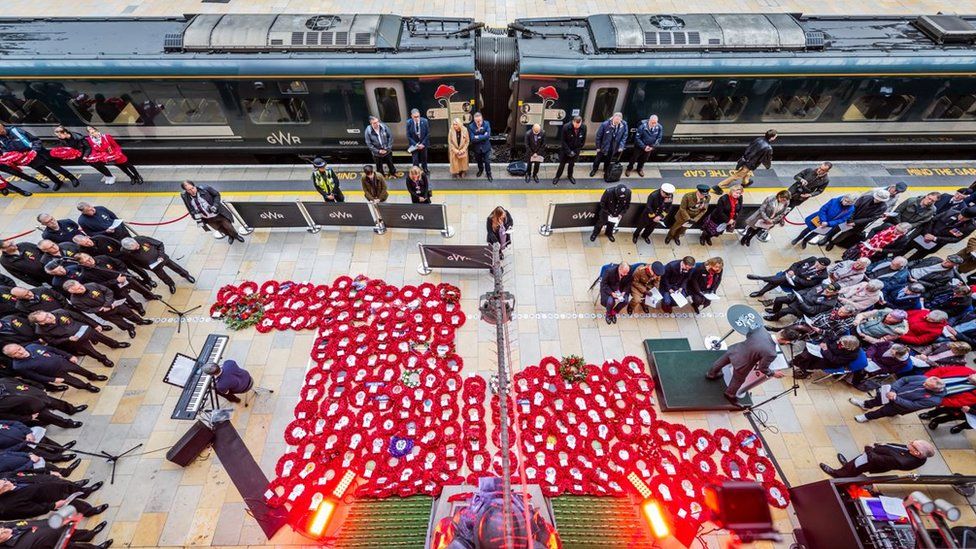 A birds eye view from above the Unknown soldier statue at London Paddington. There are poppy wreaths on the ground.