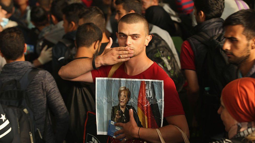 A migrant from Syria holds a picture of German Chancellor Angela Merkel as he and approximately 800 others arrive from Hungary at Munich Hauptbahnhof main railway station on September 5, 2015