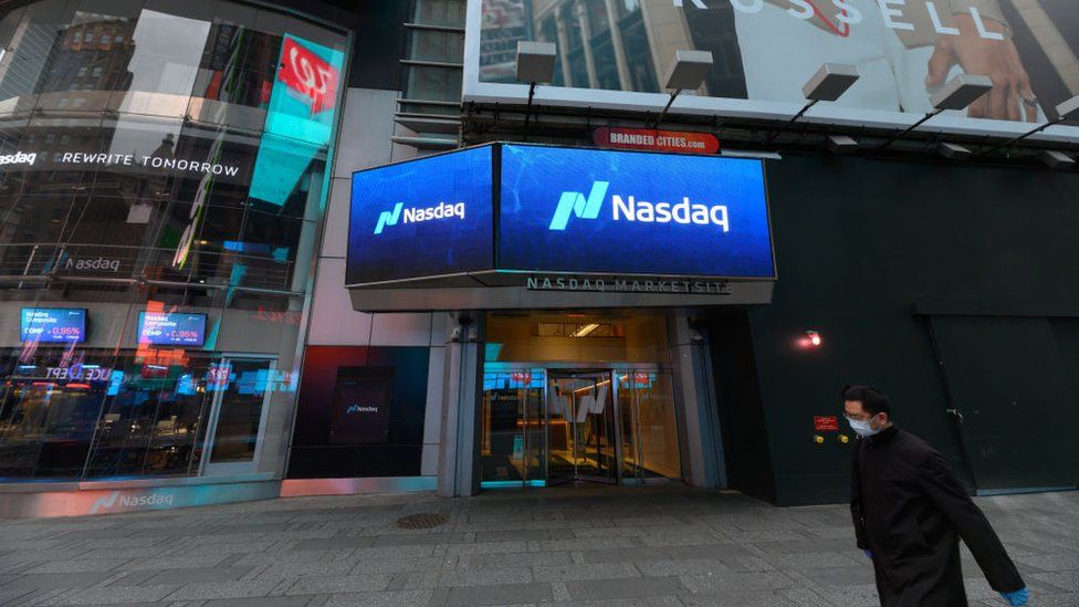 A man in a mask walks past the Nasdaq stock exchange in New York