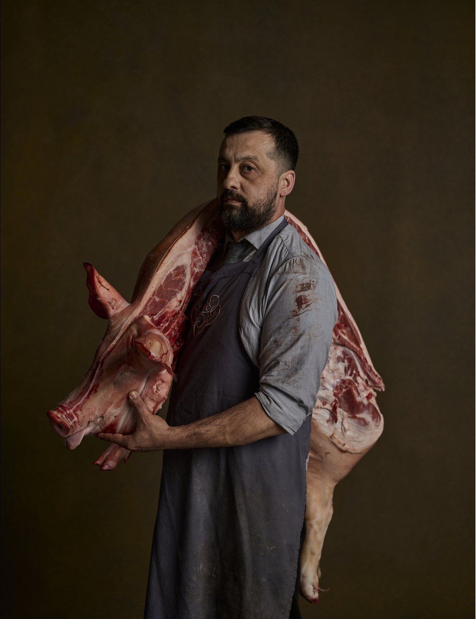 A butcher stands with a pig's carcass slung over his shoulder