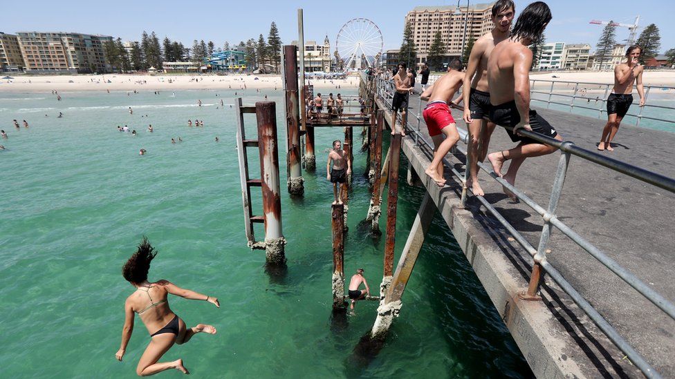 Teenagers jump off the jetty at Glenelg beach in Adelaide during a heatwave