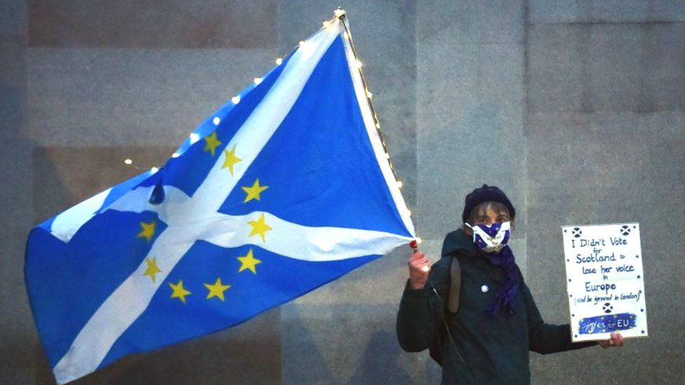 An anti-Brexit pro-Scottish independence activist holds a flag mixing the EU flag and the Scottish Saltire as she gathers for a small protest against Britain's exit from the European Union outside the Scottish Parliament in Edinburgh on December 31, 2020 hours before the end of the Brexit transition period