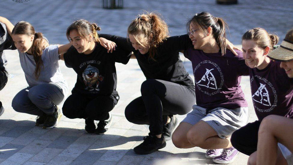 A group of women kneeling down beside each other and smiling, with their arms around each other