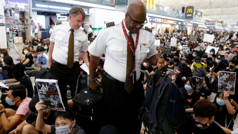 Airline staff climb through protesters gathering on the floor