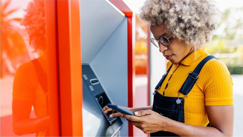 A woman looks at her phone while at an ATM