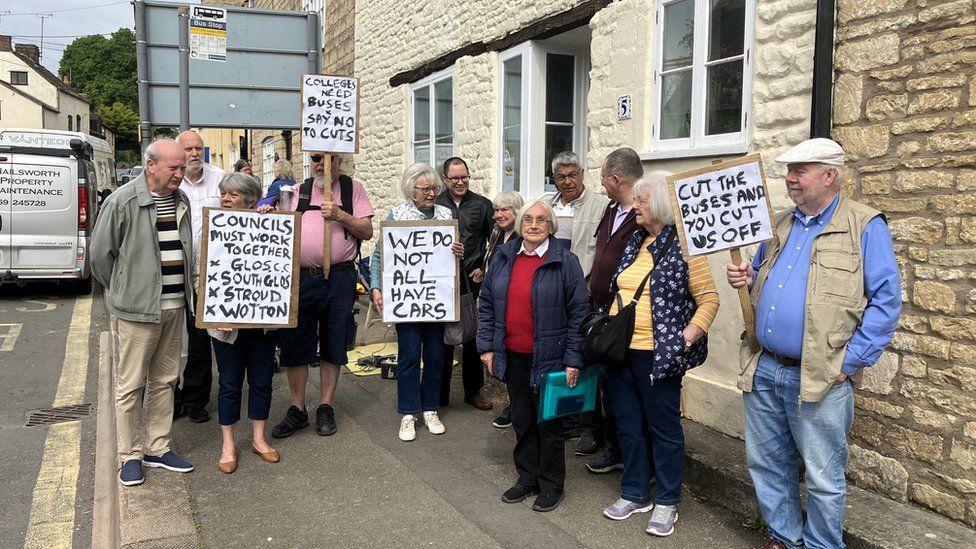 A group of elderly people holding signs that say 'we do not all have cars' and 'cut the buses and you cut us off'