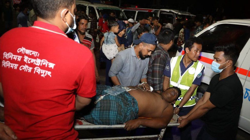 An injured man is carried to a hospital by rescue workers and civilians after a fire broke out at a container storage facility in Sitakunda