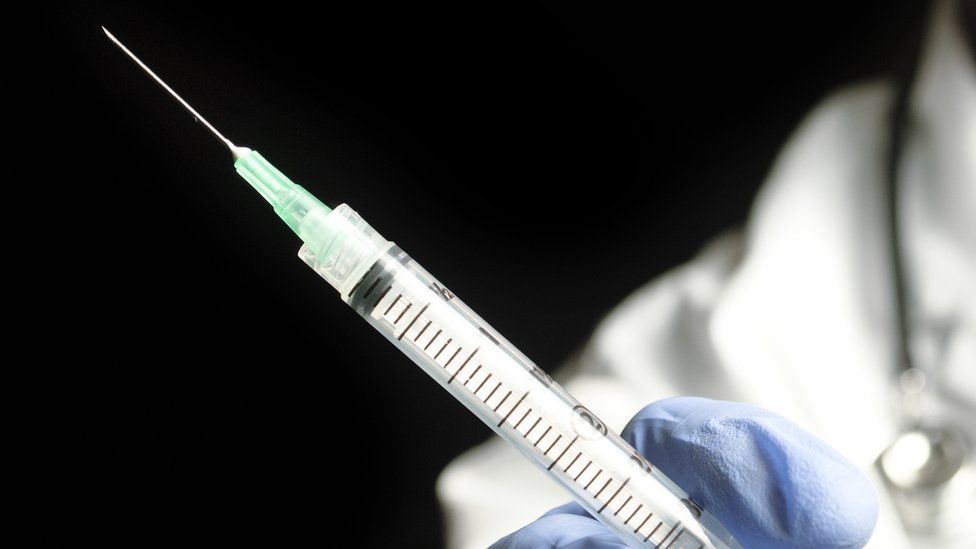 Stock image of a syringe being held in a blue-gloved hand